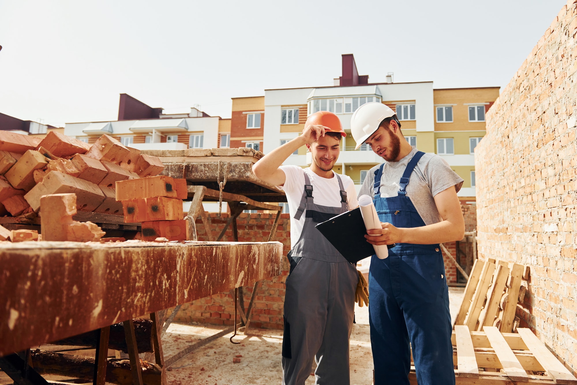 With documents. Two construction workers is together at the building