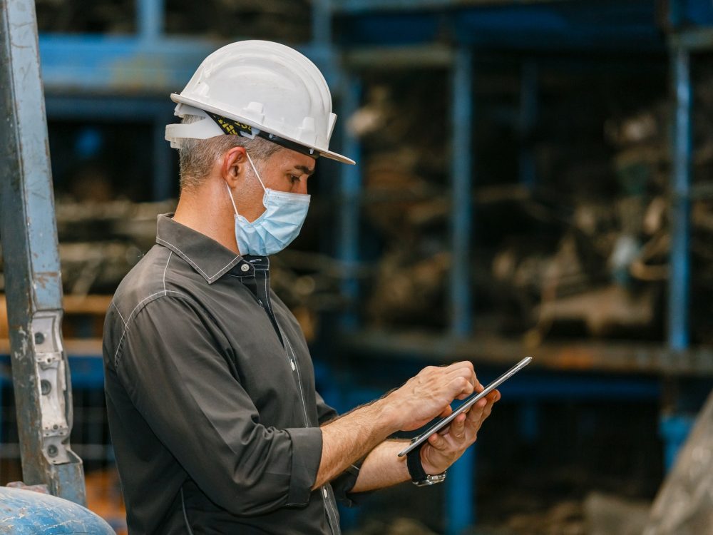 Engineering man wear face mask using tablet at factory. Heavy industry worker man concept.