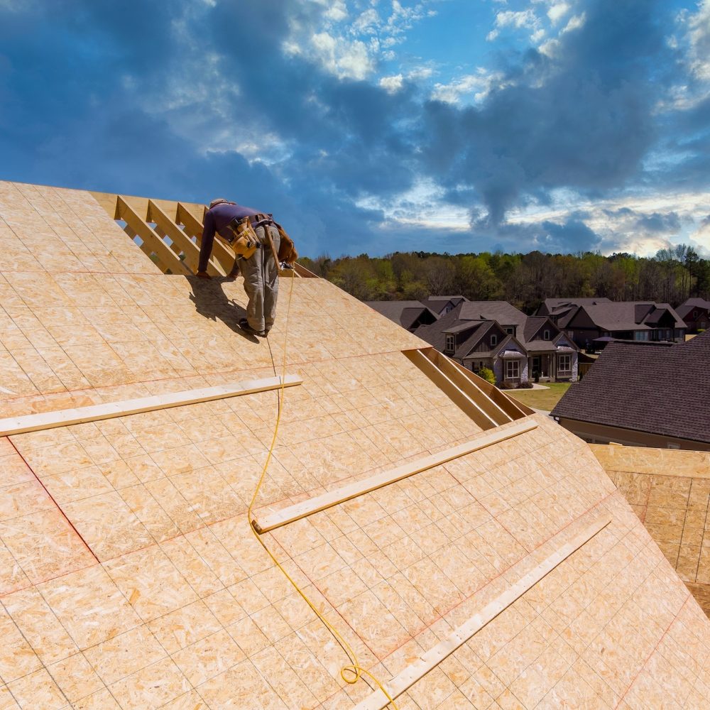 Workers build a roof on the house applying roof plywood panels